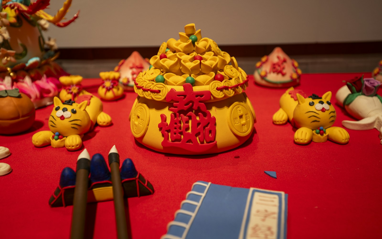 Small painted handmade clay miniatures, including tiny food and books, arranged beside brushes and paint on a craft table.