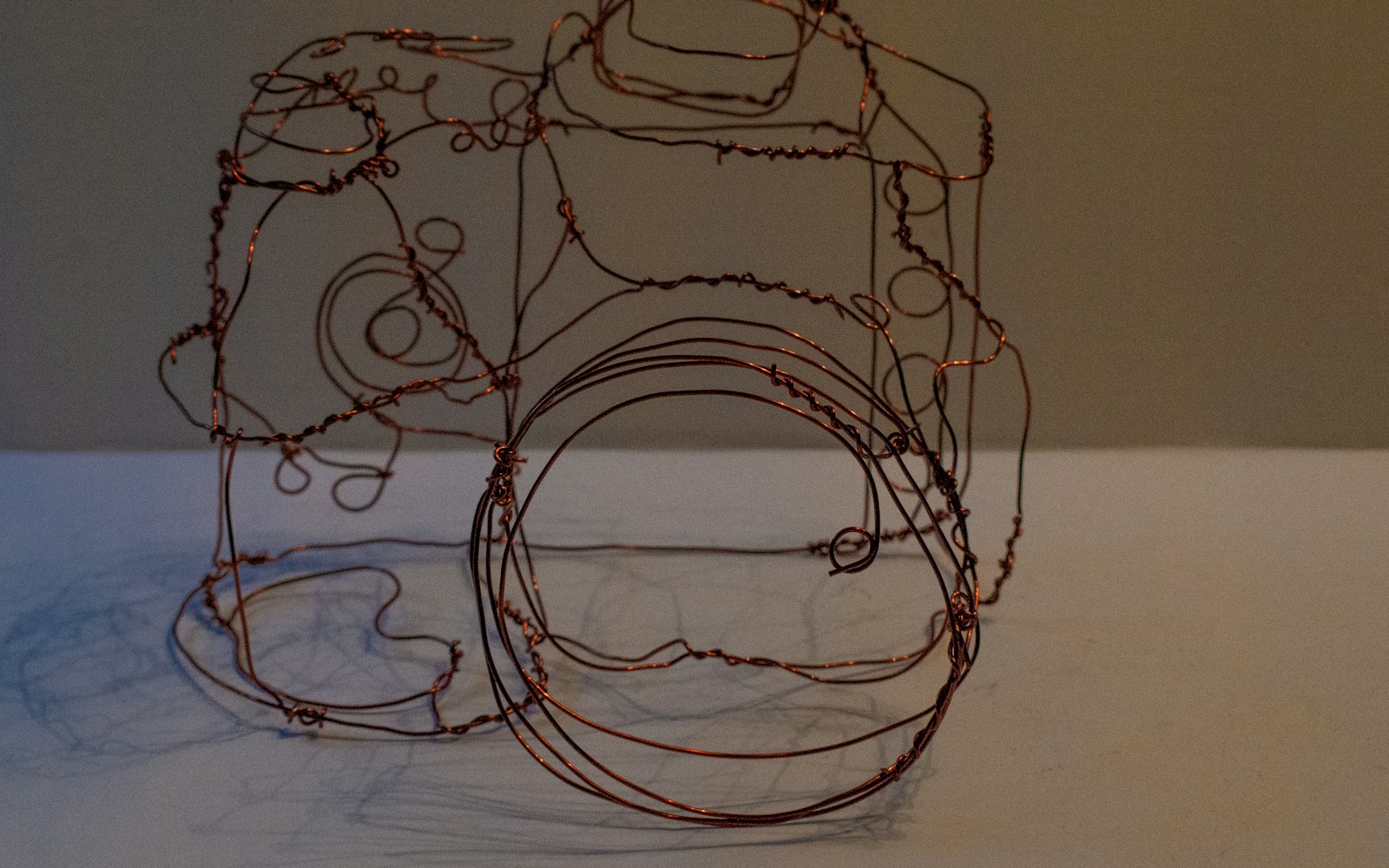 Close-up of a handmade wire armature for a small textile figure, with wrapped limbs, padding materials, pliers, and sewing tools on a worktable.