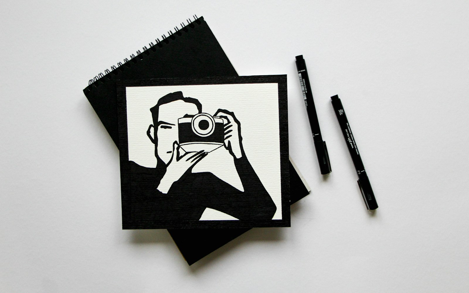 A handmade textile art doll beside a notebook, archival folders and a camera on a worktable