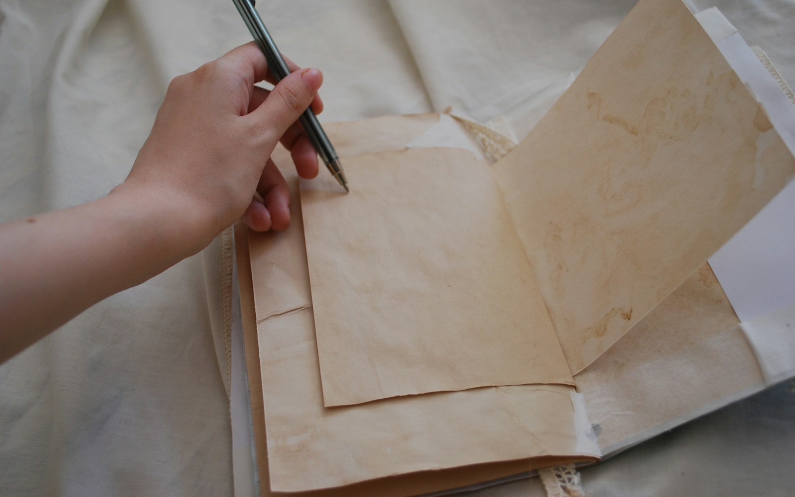 A handmade mixed-media art doll beside a notebook, measuring tape, camera, and archival storage box on a neutral worktable