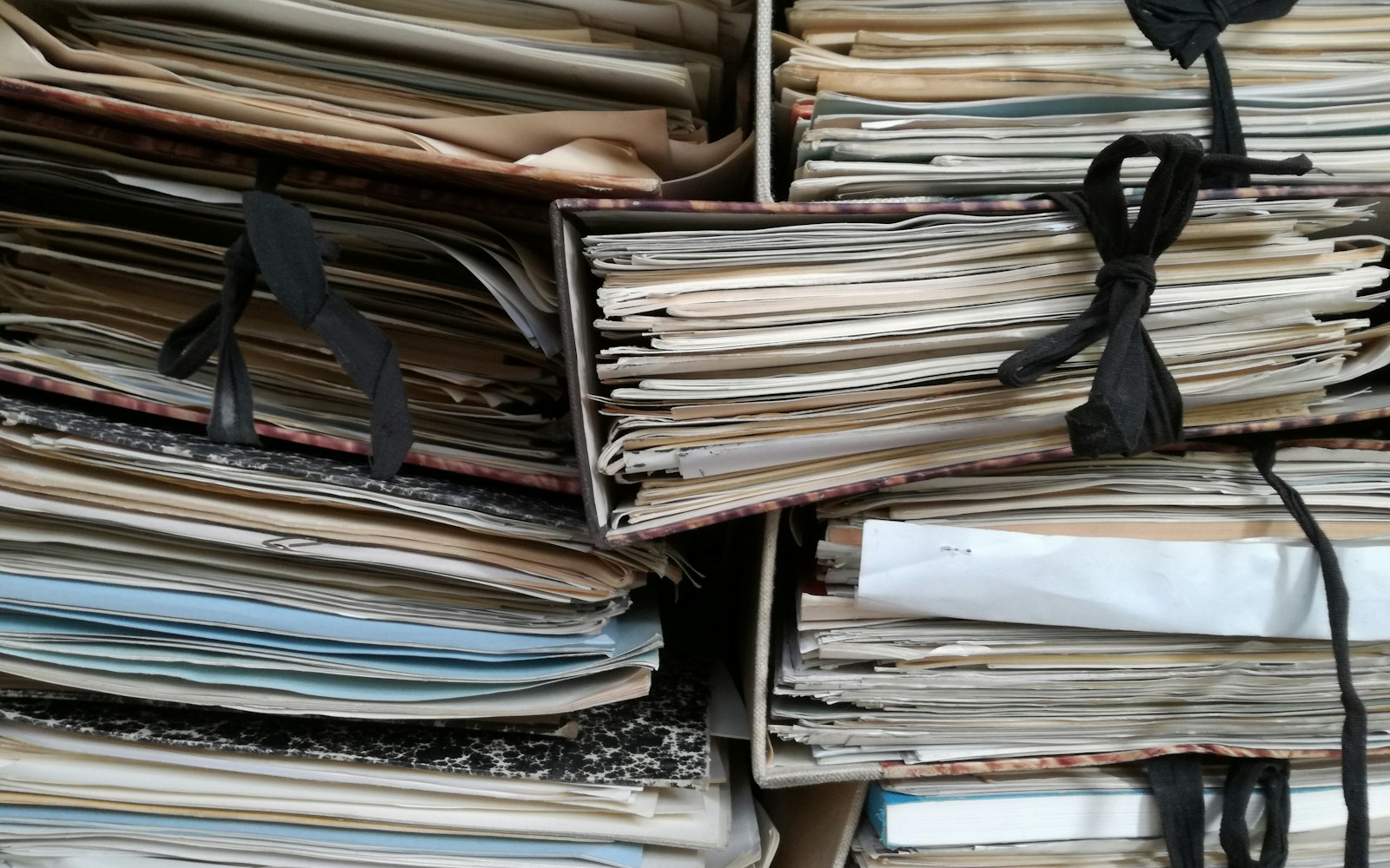 A handmade collectible doll beside archival folders, a notebook, labelled photographs, and a soft measuring tape on a clean worktable.
