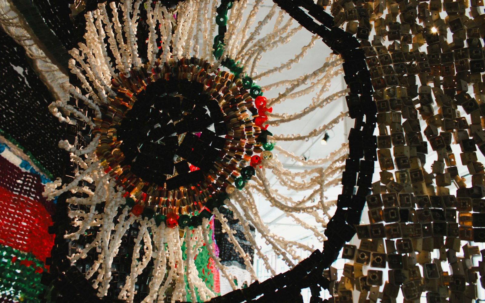 Close view of a handmade textile doll head with subtly embroidered eyelids, beaded eyes, and layered thread shading on a work surface.