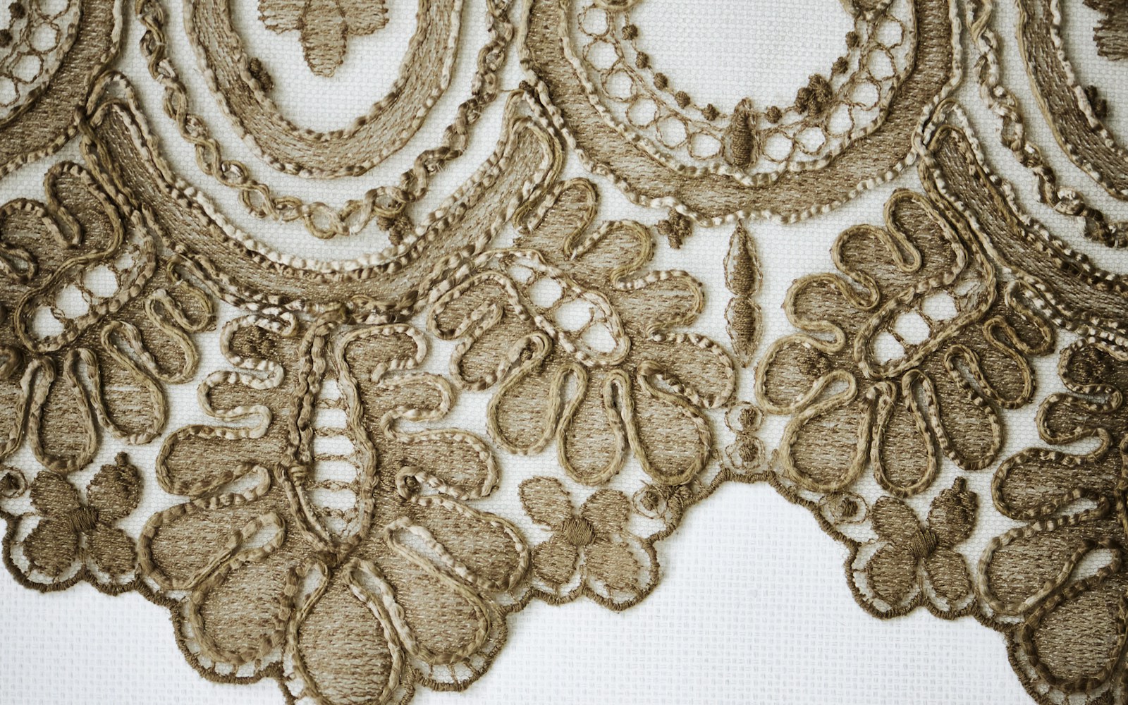 Close view of hands sewing small glass beads onto a handmade textile art doll beside thread, needles, and loose beads.