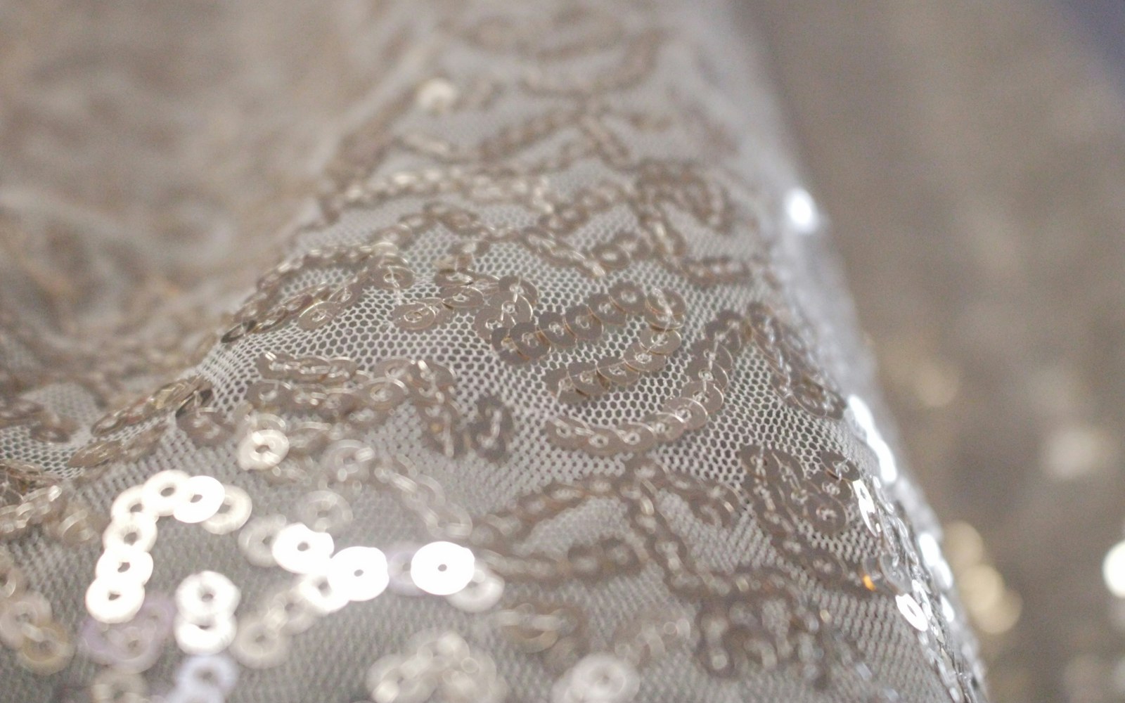 Close view of a handmade textile art doll with delicate bead embroidery, sequins, and stitched floral details on a fabric costume panel.