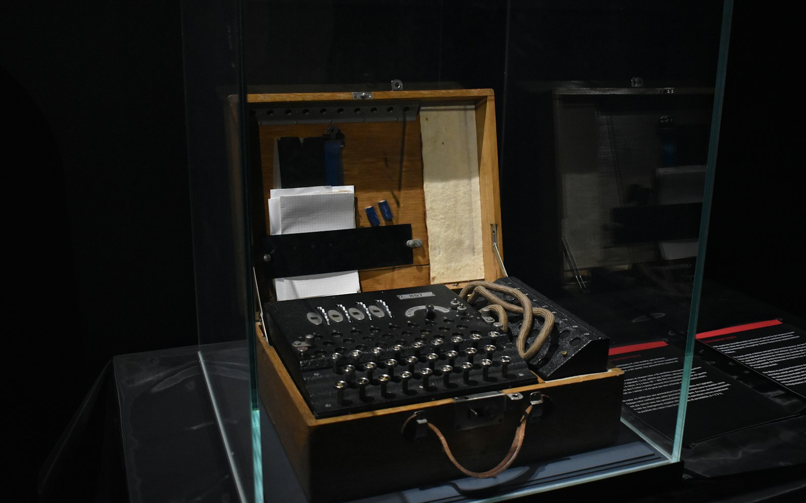 A small embroidered textile figure standing on a neutral support inside a clear protective display case