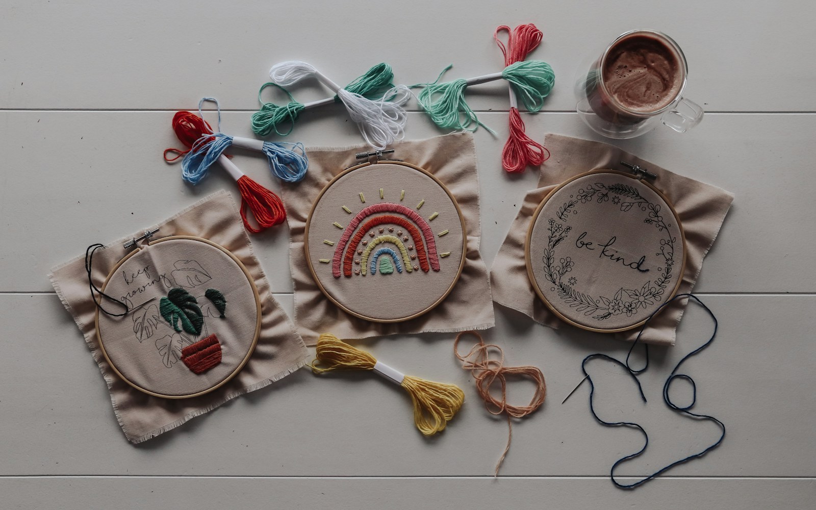 Close view of an embroidered textile doll face in progress beside thread, a fabric swatch, chalk, and marking tools on a worktable.