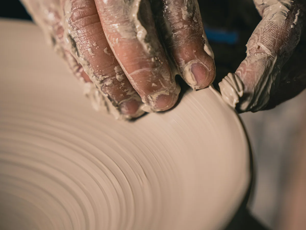 Hands shaping wet clay on a pottery wheel.