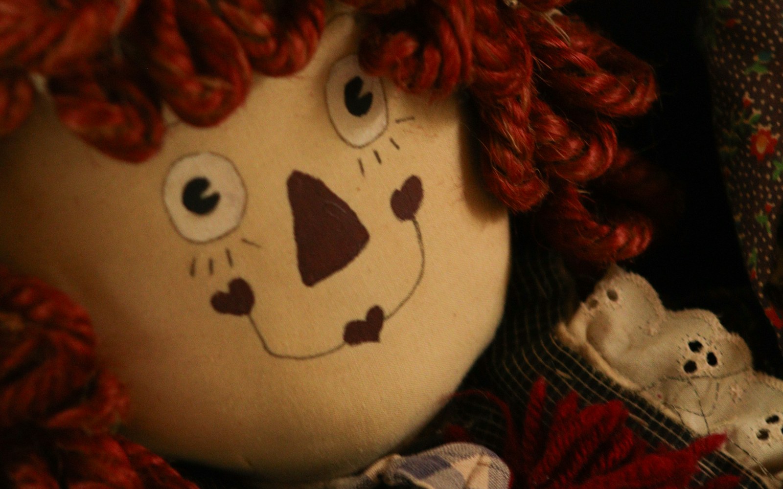 Close view of a textile art doll face with embroidered eyes, beads, and layered fabric relief
