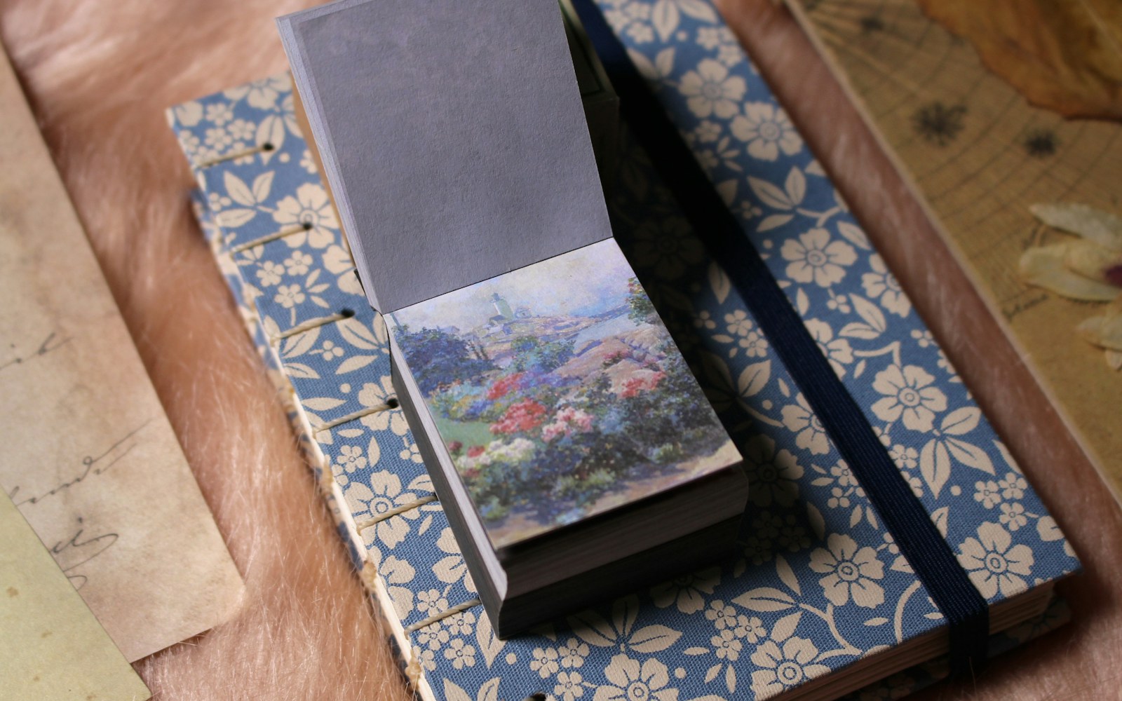 A handmade miniature dollhouse photographed beside a notebook, ruler, pencil, and archival paper sleeves on a clean work surface.