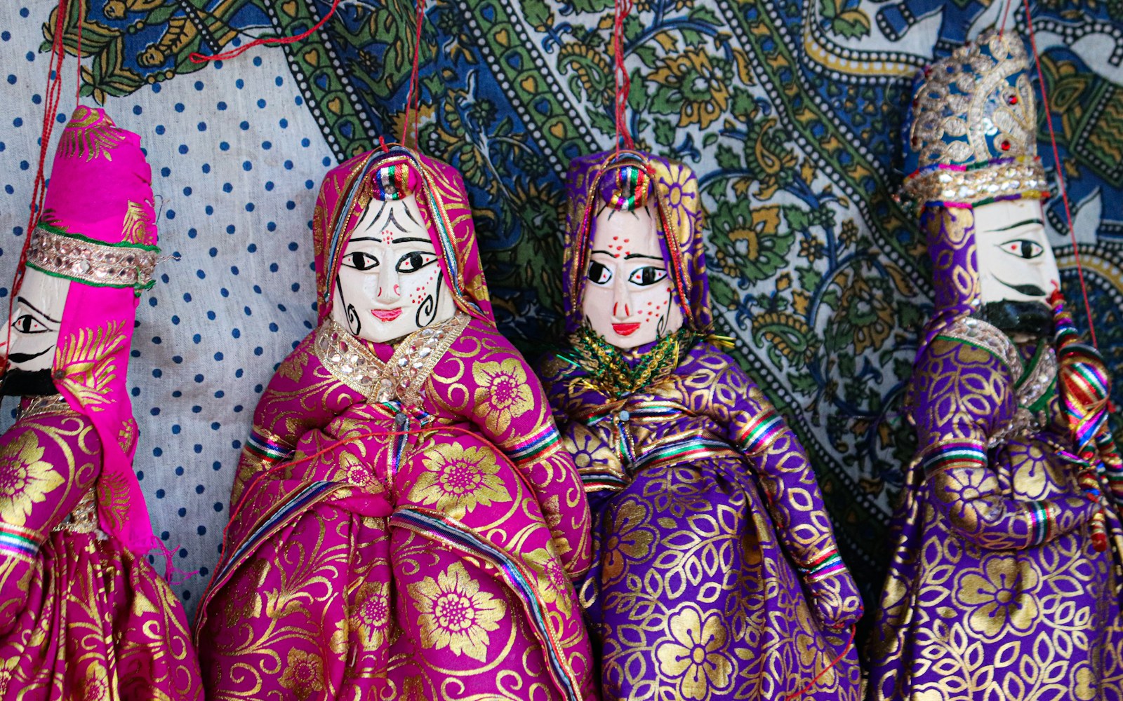 Close editorial view of a textile doll face with fine embroidered eyes, a stitched mouth, small beads, and embroidery threads on a work surface