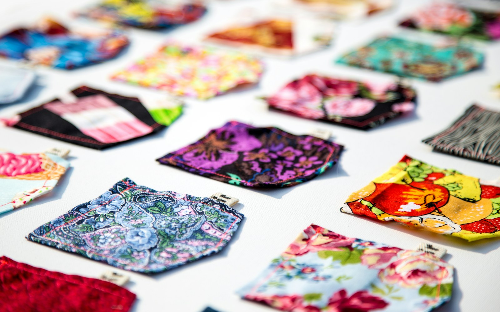 A small handmade doll wearing a partially fitted textile costume beside paper pattern pieces, fabric swatches, and sewing tools.