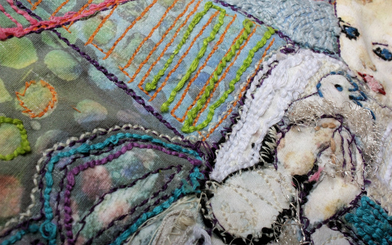 Close editorial view of a textile figure under construction, showing embroidered fabric being secured over layered padding and a small wire armature.
