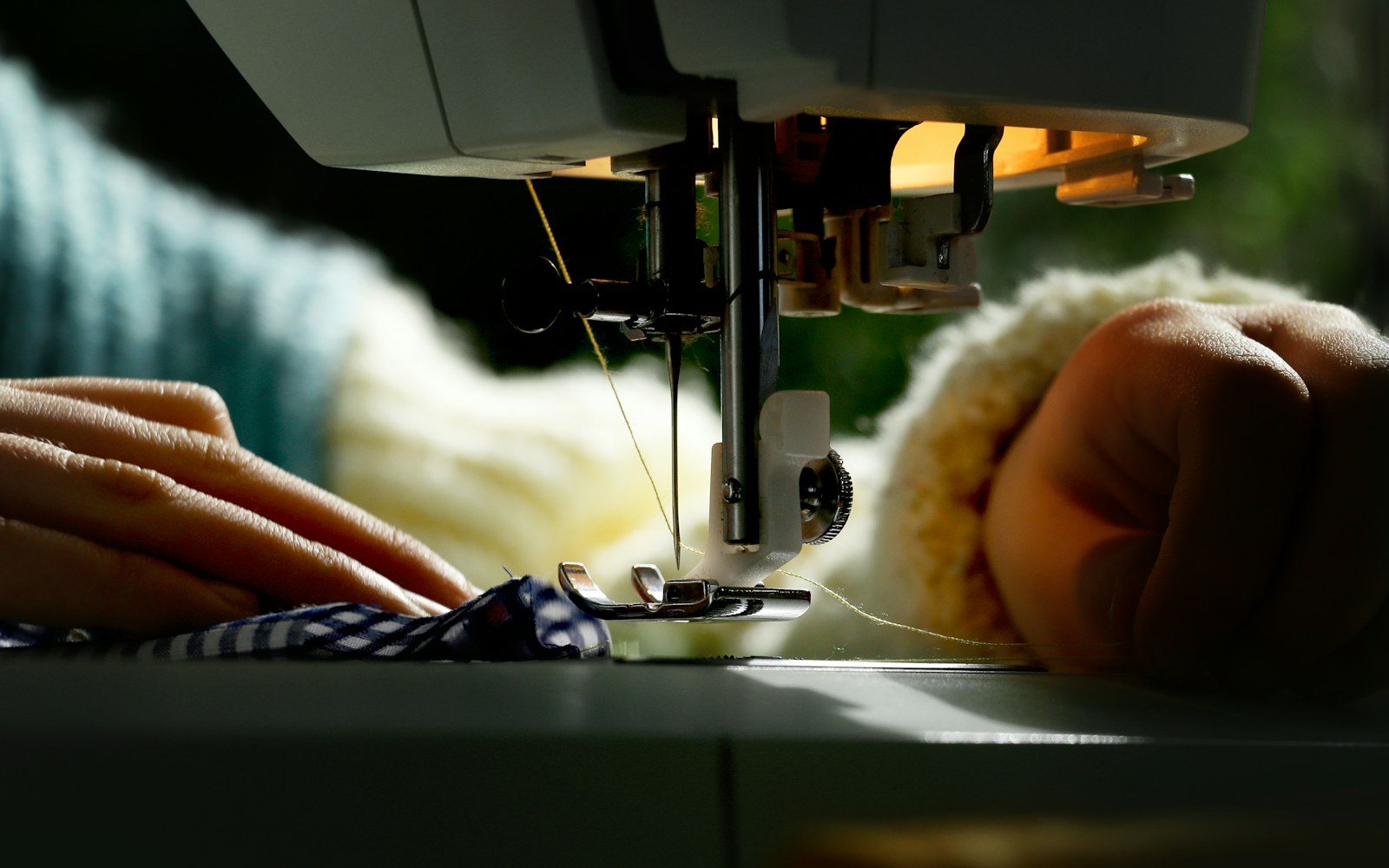 Hands shaping a small hand-stitched textile figure beside fabric scraps, stuffing, thread, and a simple wire armature.