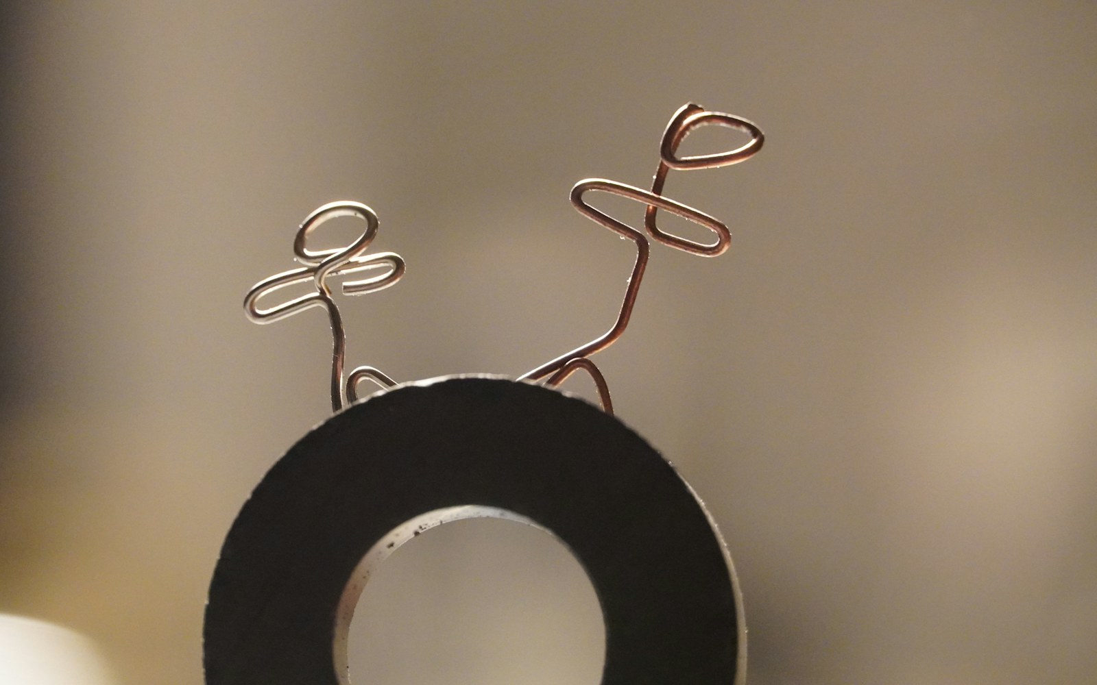 Close view of a handmade wire armature shaped into two legs, feet, hips, and a spine on a craft worktable.
