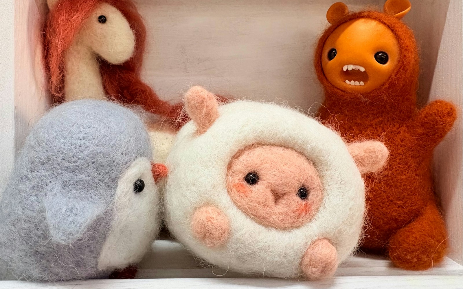 Hands arranging wool fibres beside a small handmade felted animal figure and reference photographs