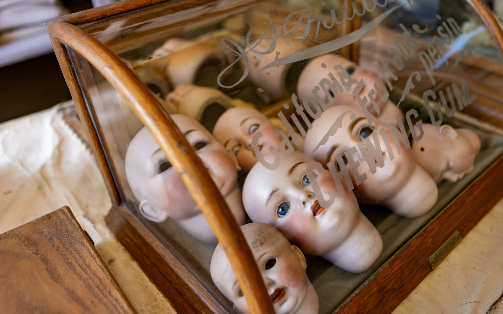 A delicate handmade art doll with glass and textile details displayed on a stable shelf inside a clear protective case away from direct sunlight