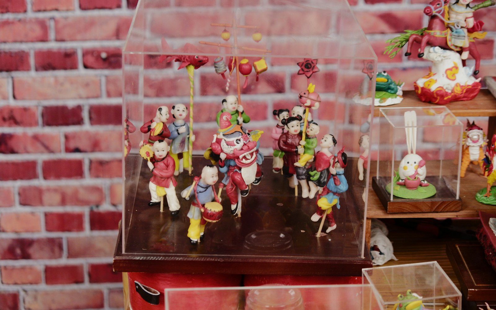 A mixed-media art doll displayed on a padded stand inside a clear case away from direct sunlight