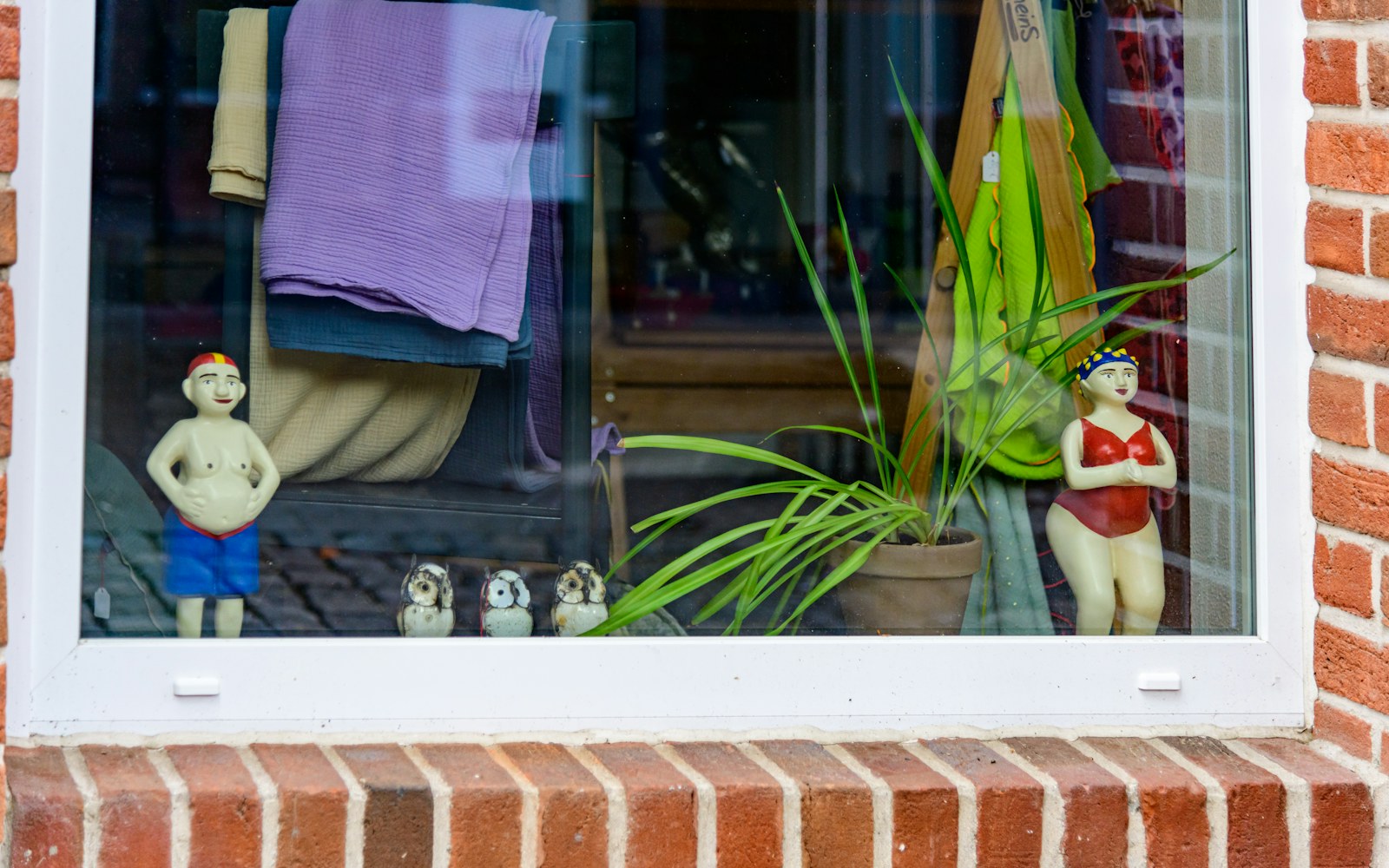 A delicate freestanding embroidered textile figure displayed inside a clear protective case on a stable shelf