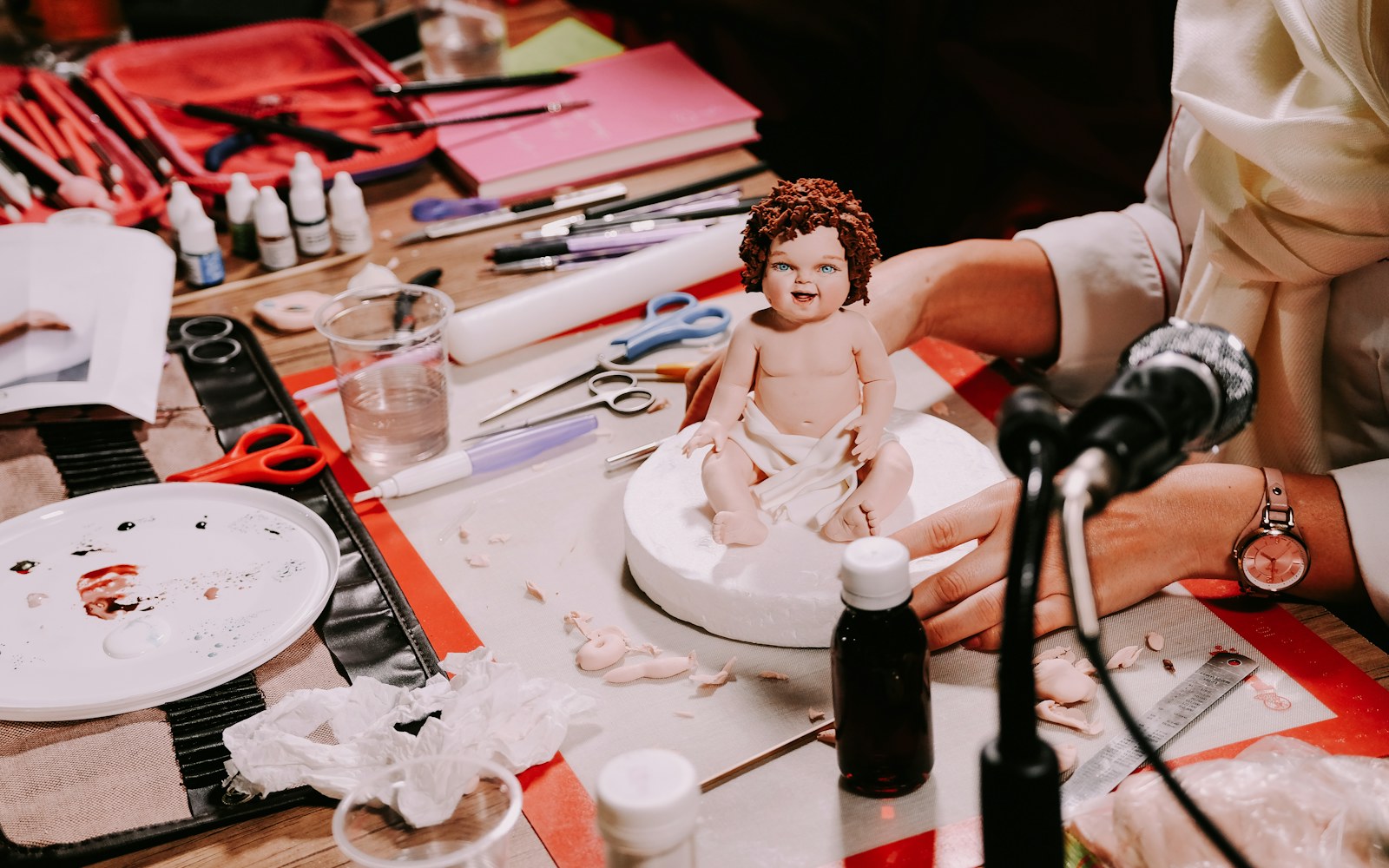 A handmade art doll beside a notebook, measuring tape, camera, and archival storage folder