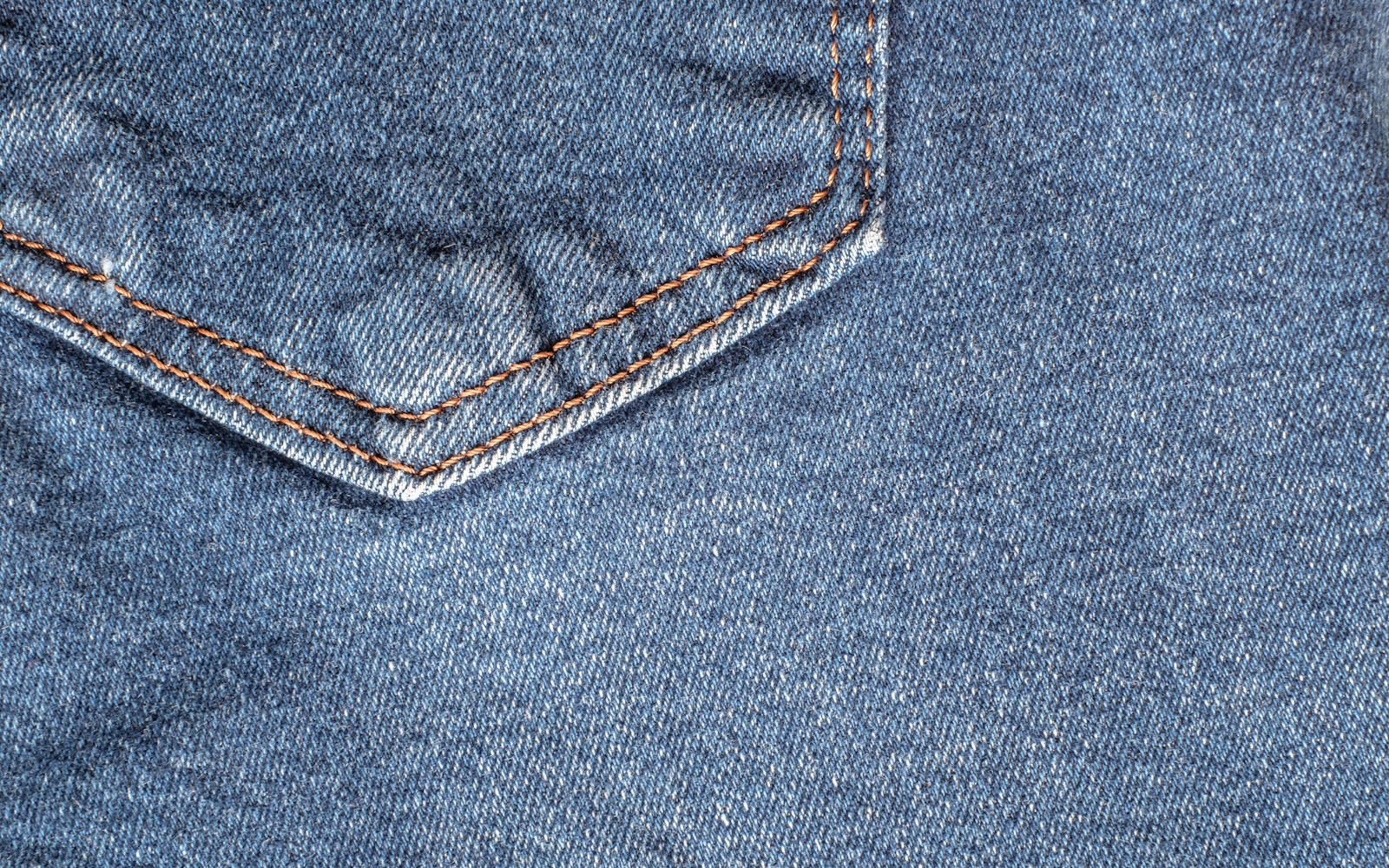 Close view of reclaimed denim, printed packaging, thread, labels, and handwritten material notes arranged on a worktable beside a handmade textile doll.