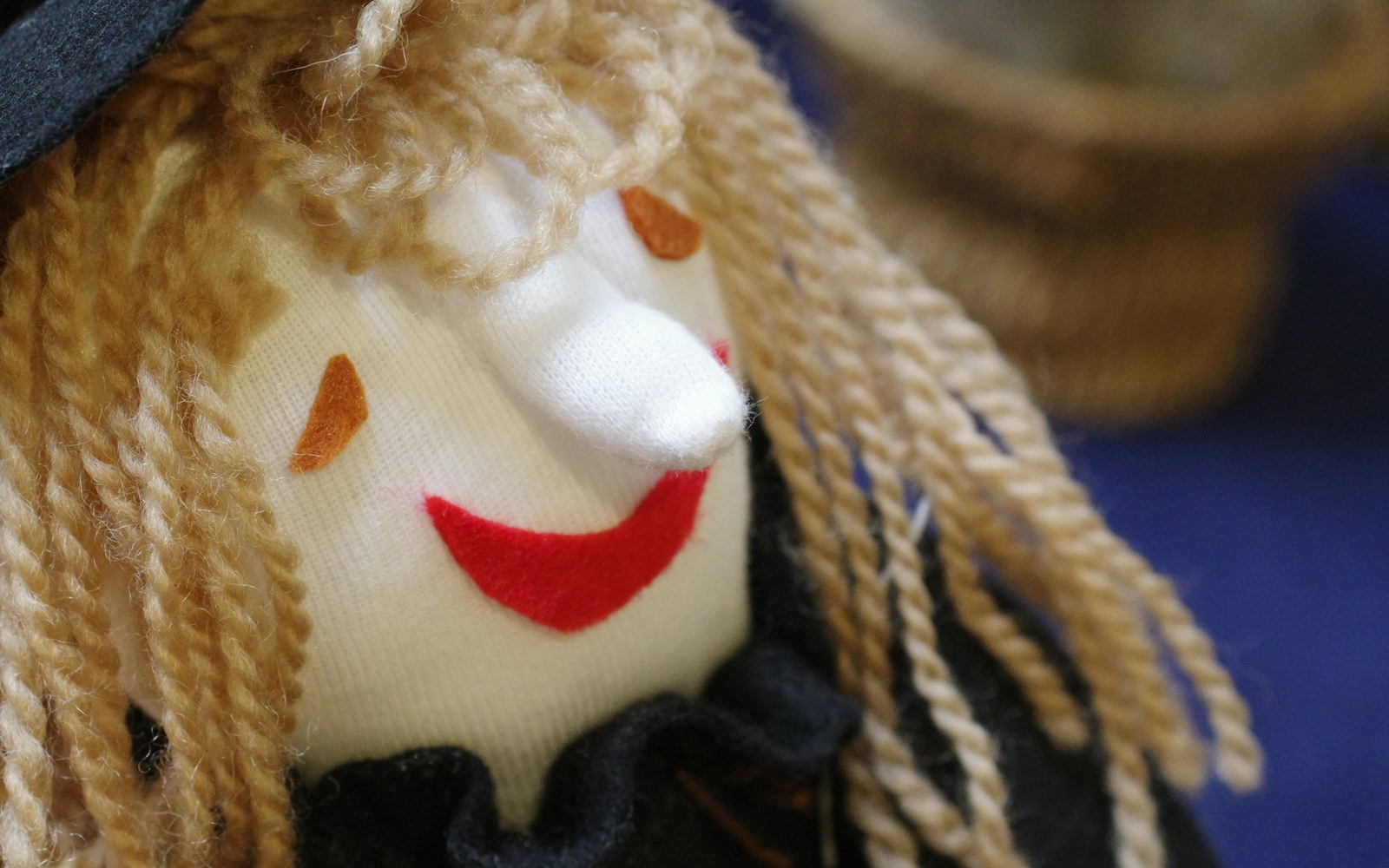 Close view of an art doll face with layered embroidered eyes, visible thread direction, and a needle resting beside the work.