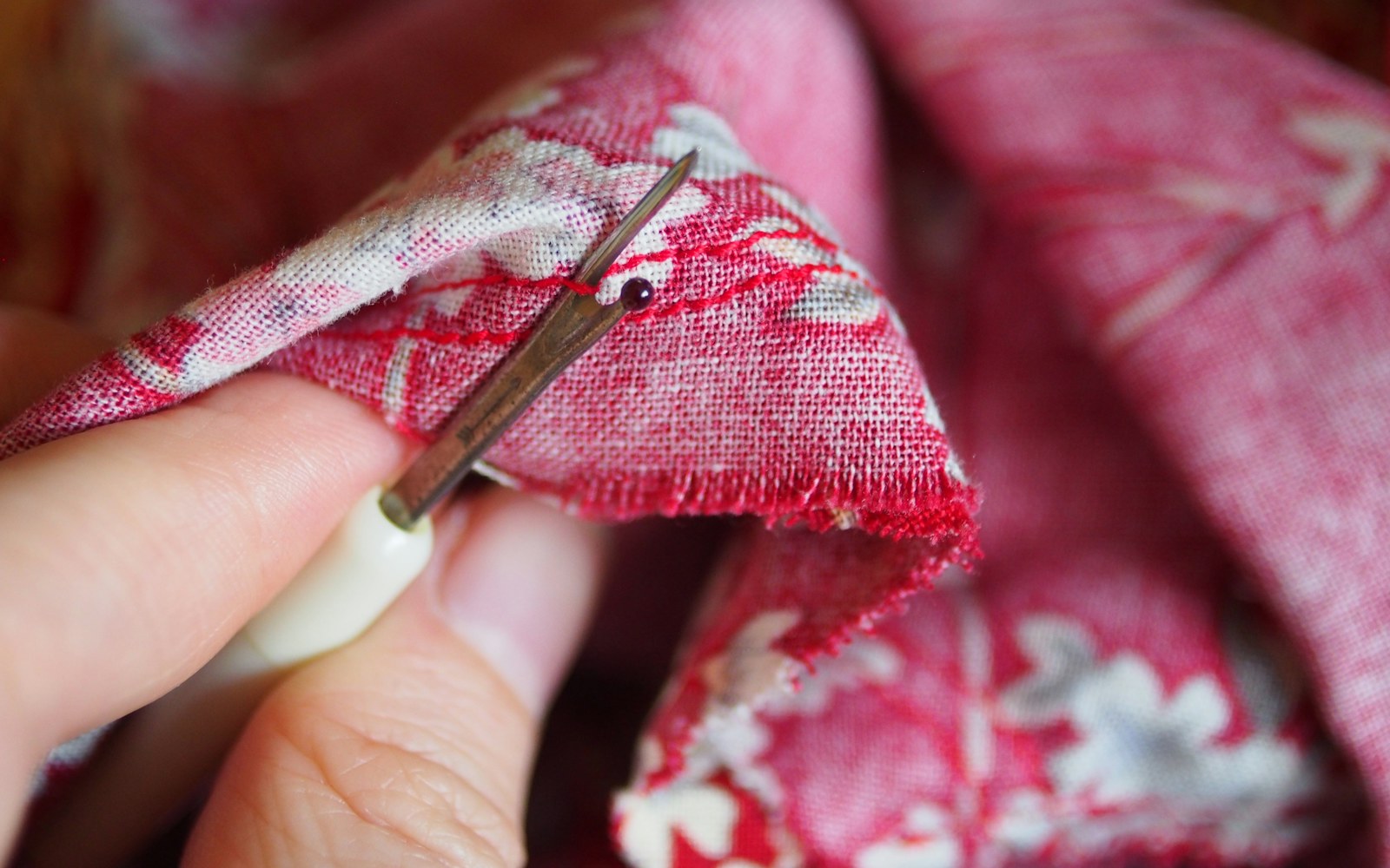 Close view of small fabric scraps, paper garment pattern pieces, thread, scissors, and a partially sewn miniature doll dress on a worktable.