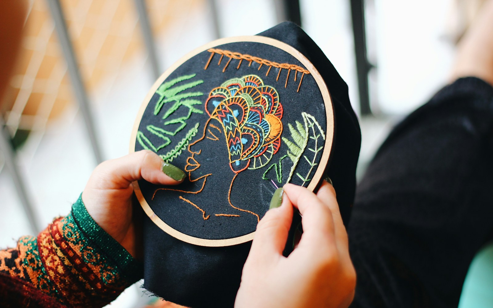 Close view of a small fabric leaf being shaped around a fine covered wire armature beside embroidery thread and sewing tools