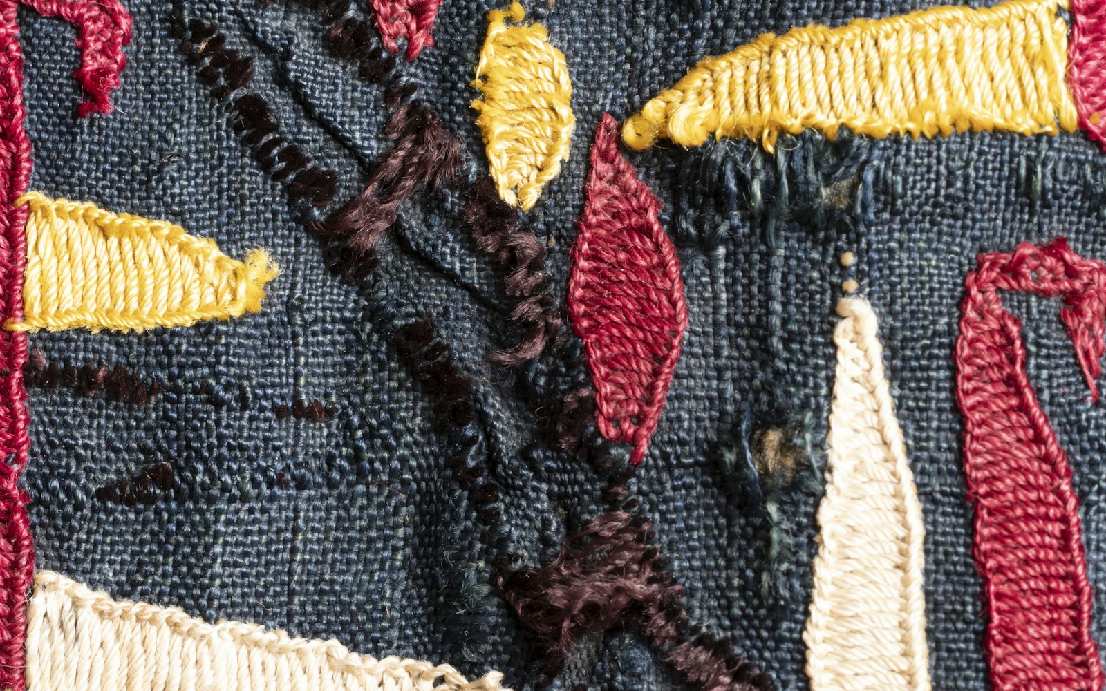 A small embroidered fabric leaf with a fine wire outline beside embroidery thread, scissors, and a handmade figure costume.