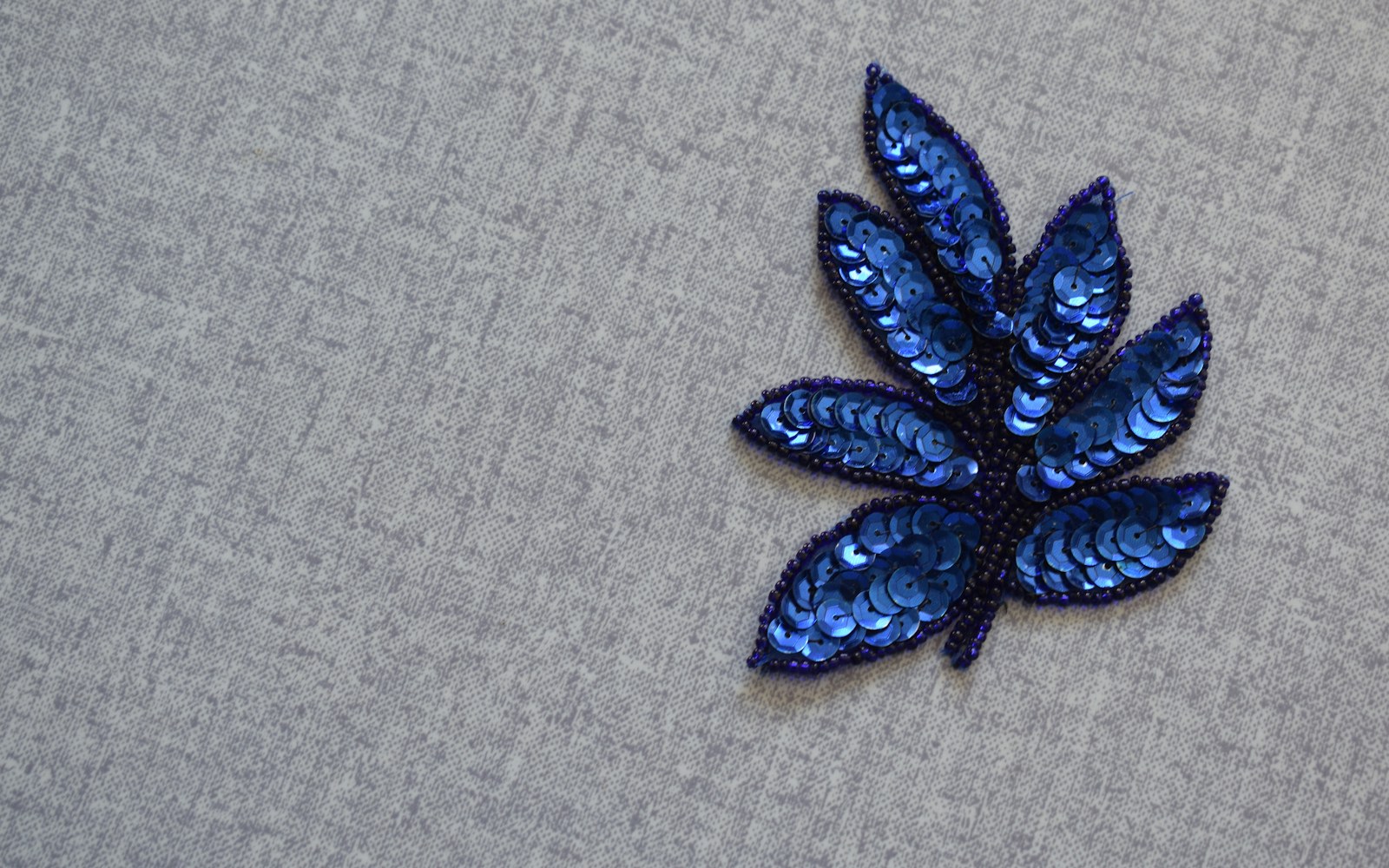 A close-up of embroidered fabric leaves with visible veins, fine wire outlines and embroidery tools on a worktable.