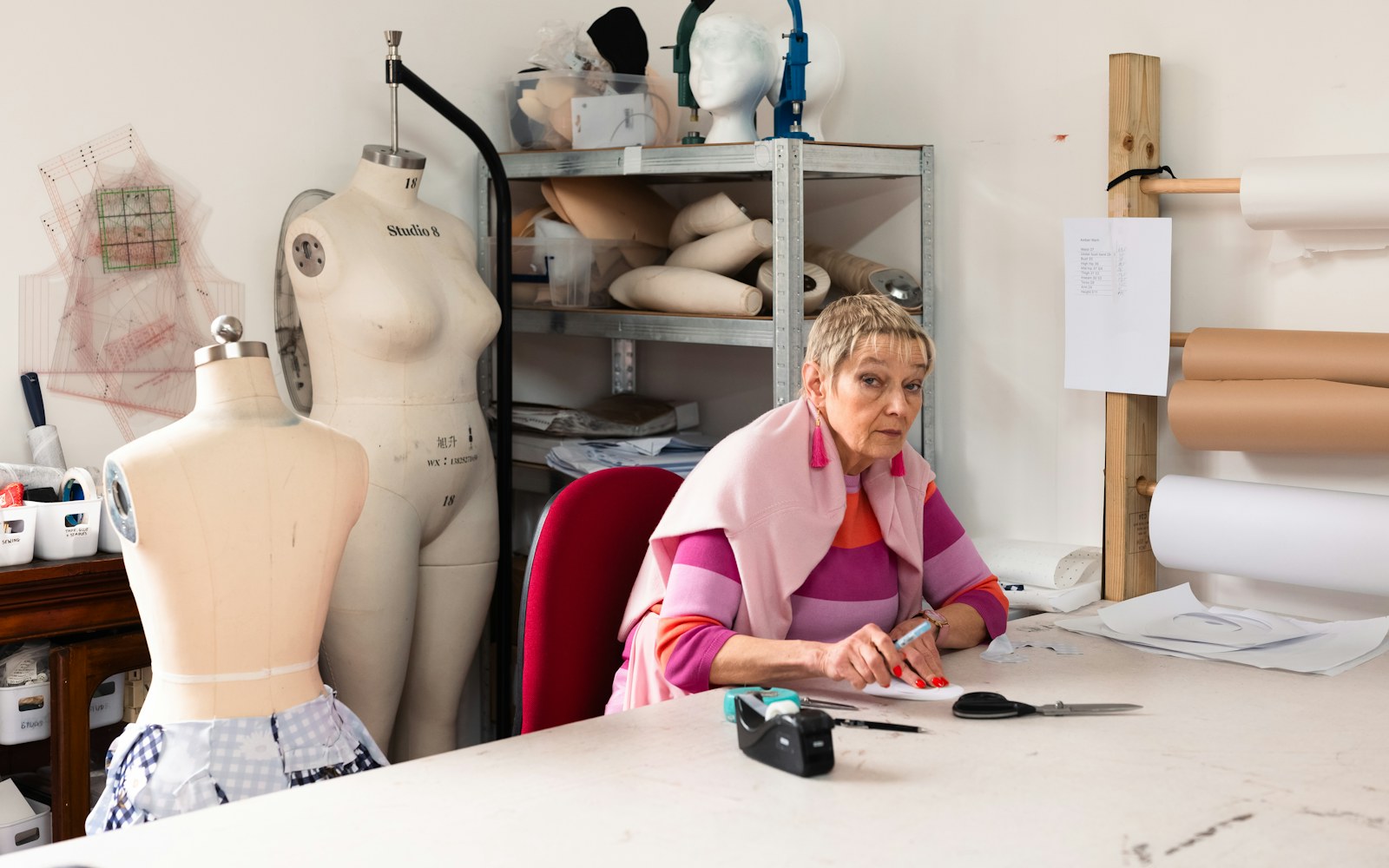 A flexible tape measure, paper pattern pieces, and a small handmade garment arranged beside an art doll on a worktable.