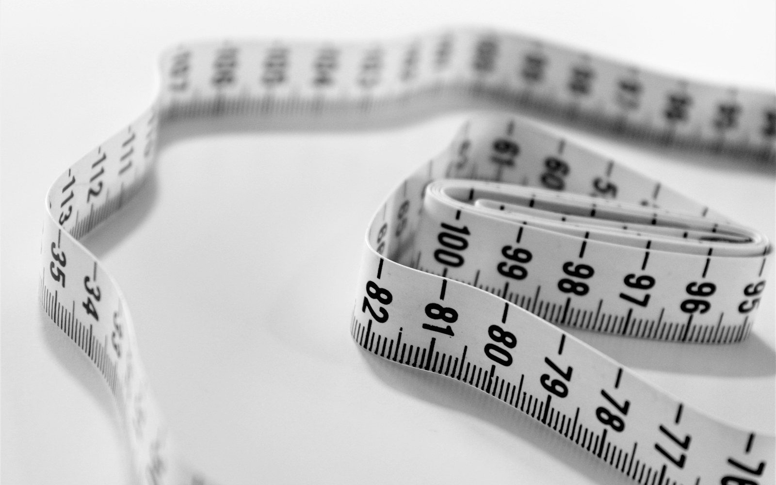 A flexible measuring tape, paper pattern pieces, and scrap fabric arranged beside a handmade art doll