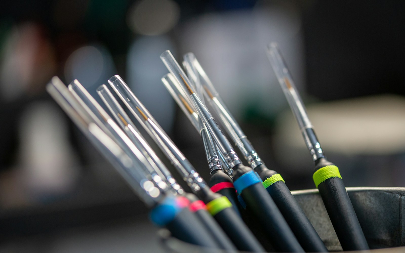 A hand holding a small painted polymer-clay figure beside soft brushes and clear finishing supplies on a clean worktable.