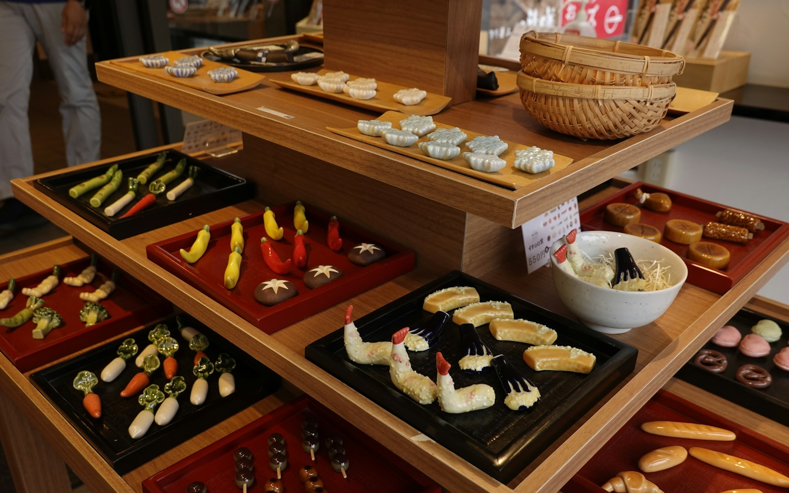 Handmade miniature pastries, fruit, cups, and paper food packages arranged beside an art doll hand on a craft table.