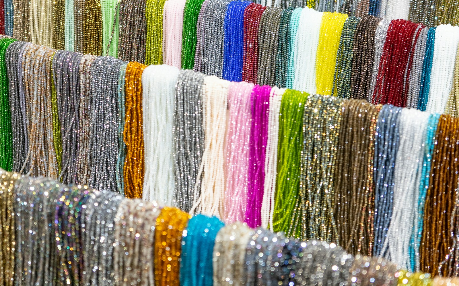 Close-up of a handmade art doll detail with fine wrapped wire, translucent textile wings, embroidery thread, and small beads on a worktable.