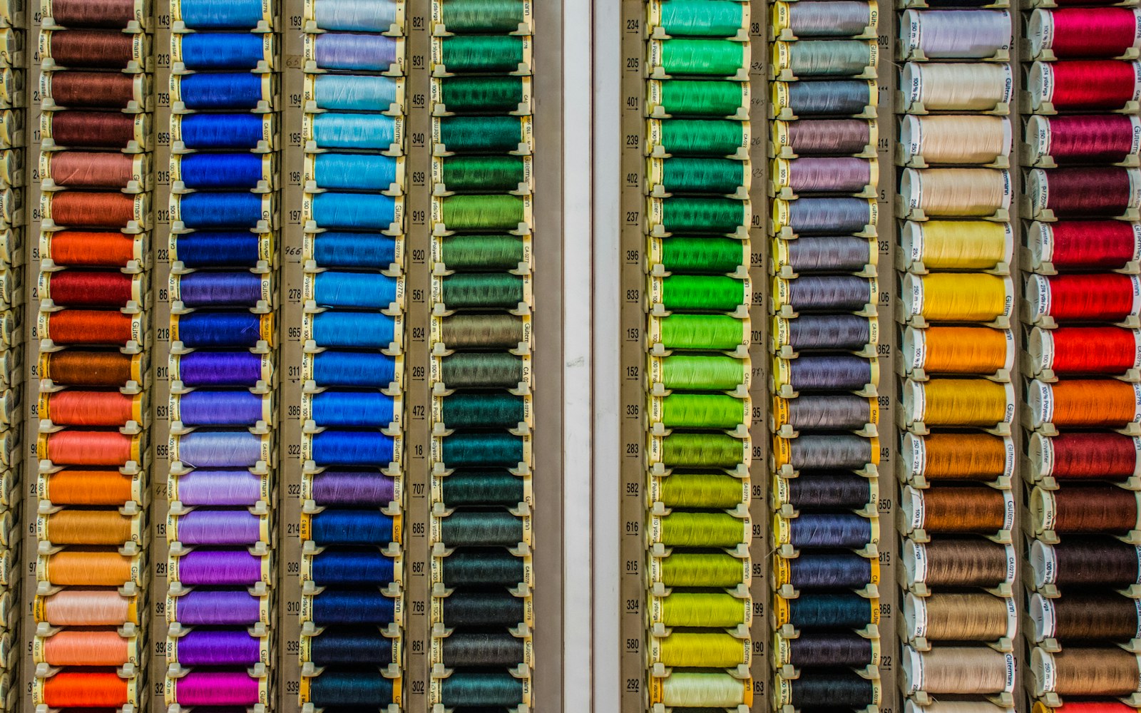 Close view of a maker stitching fine openwork lace with a needle beside a small handmade doll garment and thread spools.