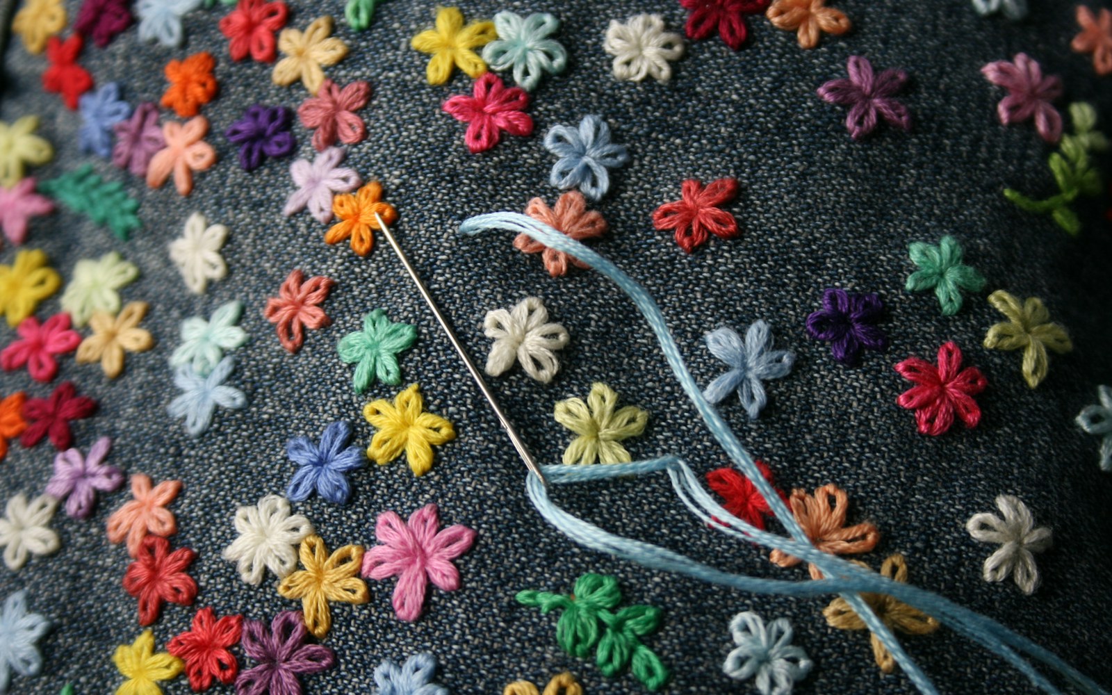 Close view of a maker stitching fine white needle lace with a small needle over a paper pattern, with a delicate wired wing shape in progress.