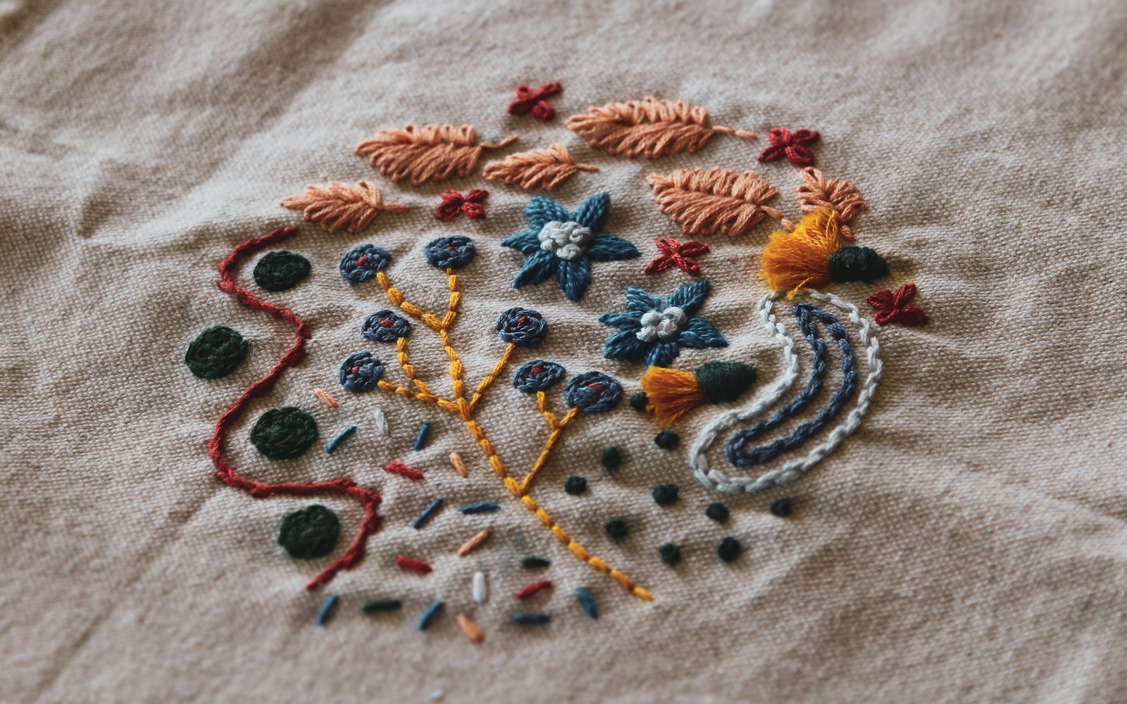Close-up of a hand embroidering a tiny floral motif on a doll dress, with a hoop and stabilizer visible