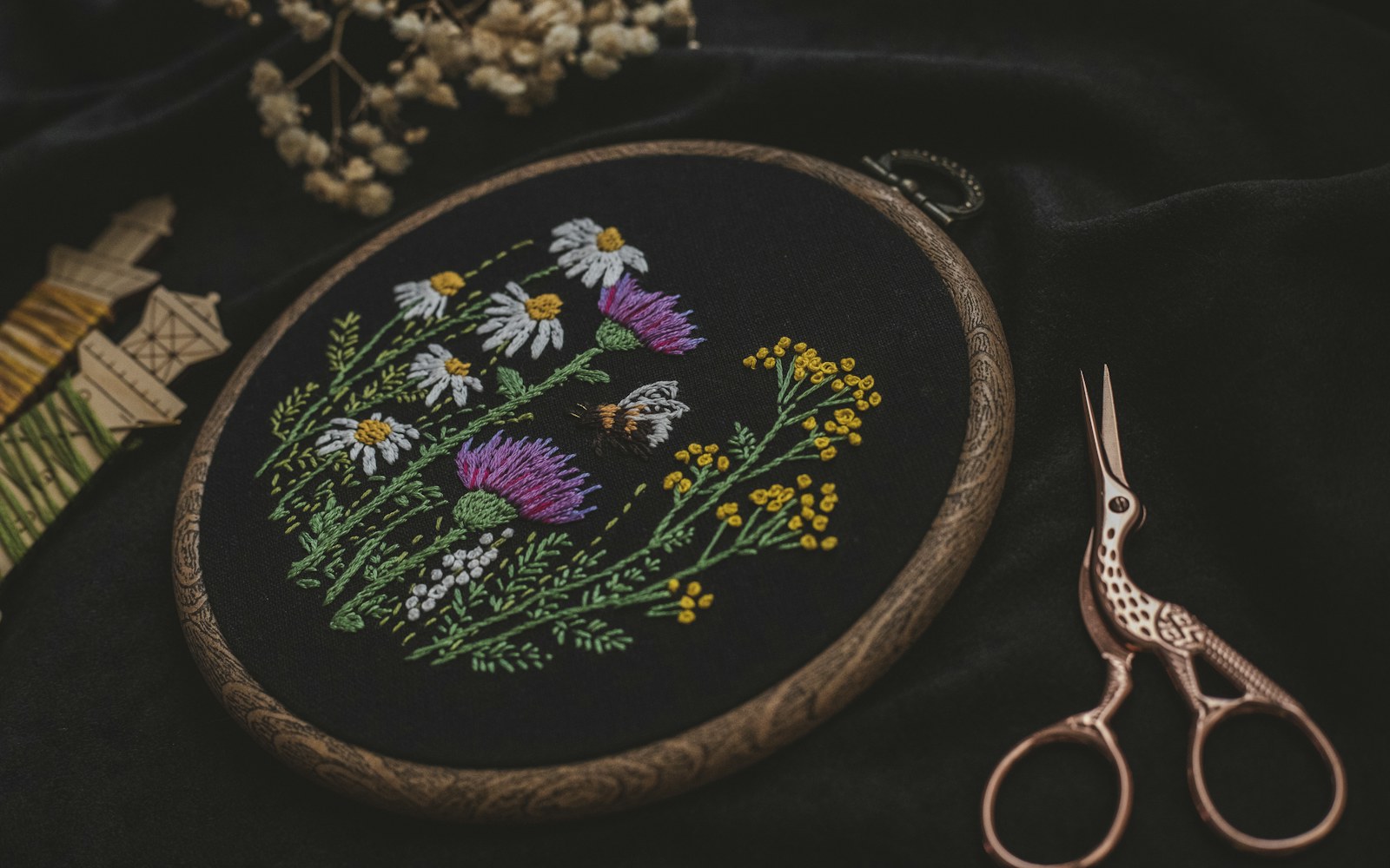 Close view of embroidered miniature leaves and flowers being shaped around fine covered wire beside an art doll