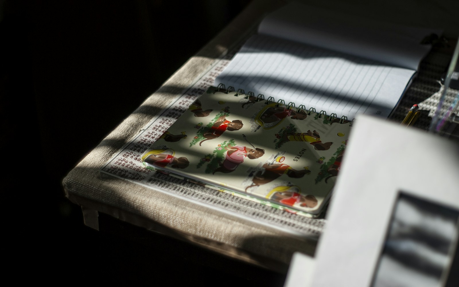 A handmade art doll beside a notebook, measuring tape, camera and archival storage folder on a worktable